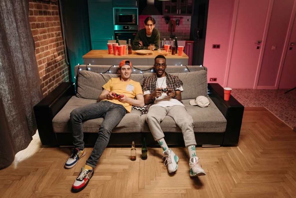 Three friends enjoying a gaming night in a cozy living room with colorful lights and drinks