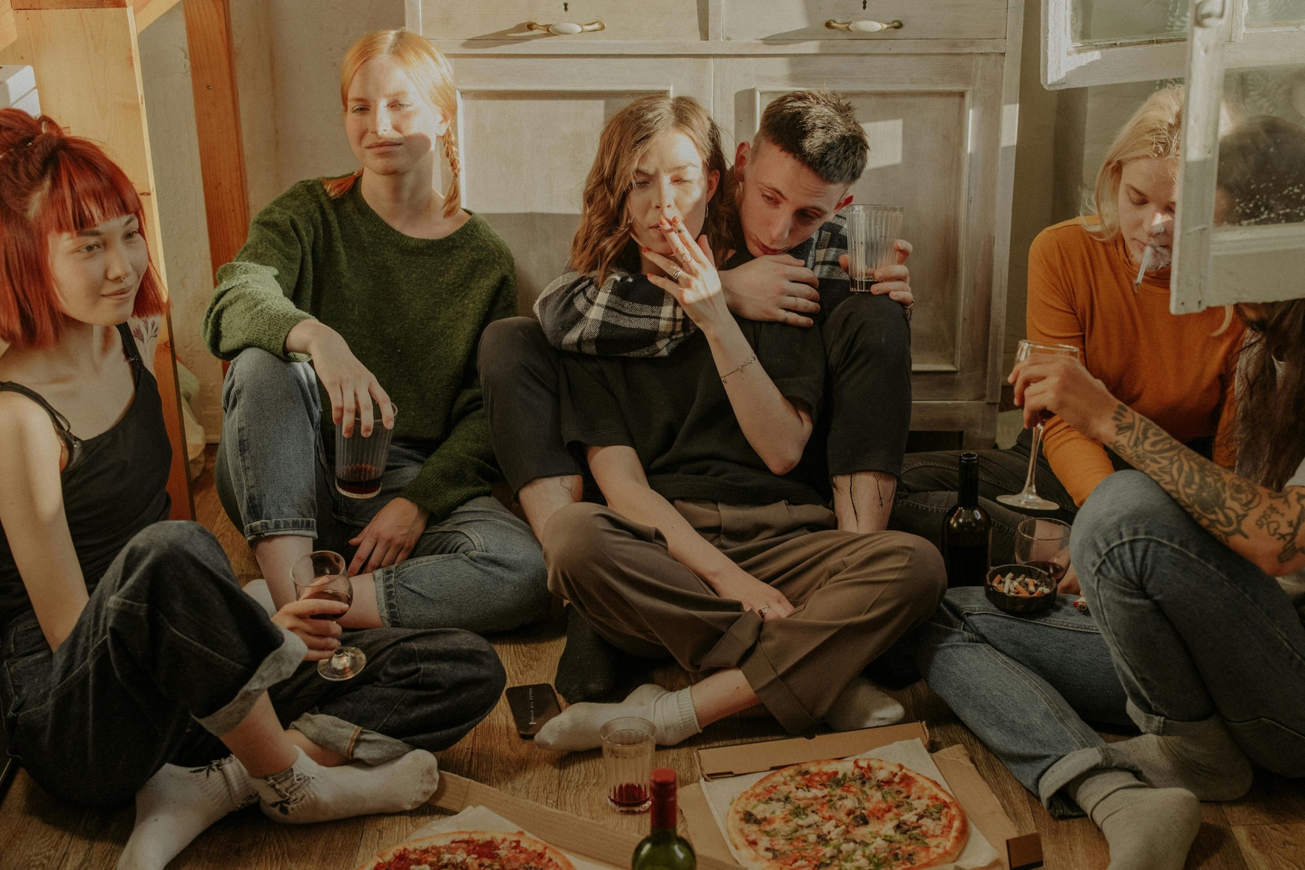 Group of flatmates sitting on the floor sharing pizza and drinks